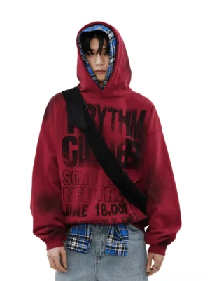 Burgundy red Rhythm Clash oversized graphic hoodie with distressed black typography, blue plaid hood lining, spray-faded texture, layered plaid shirt, jeans, and crossbody bag