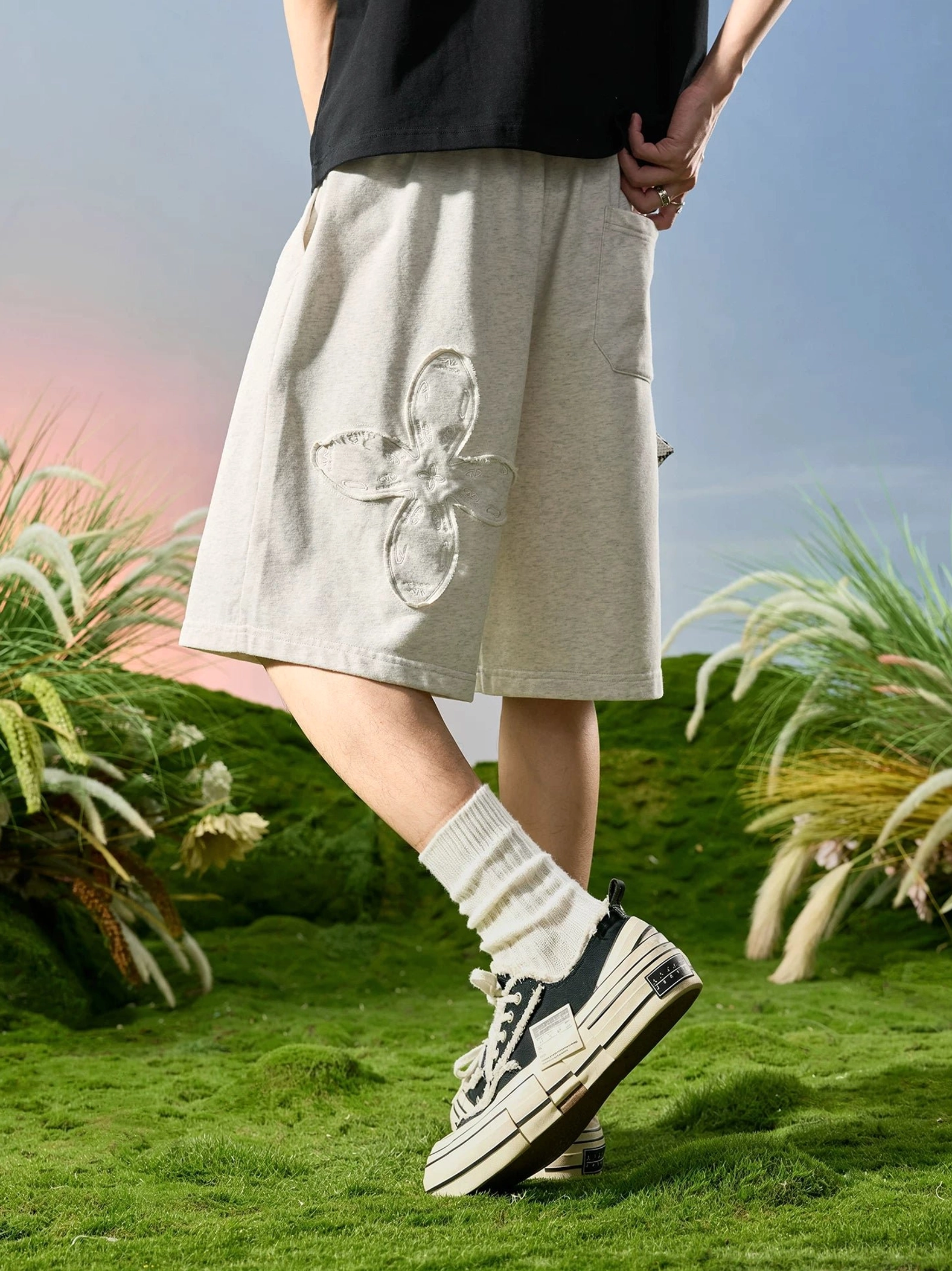 Rice gray floral appliqué relaxed sweat shorts shown in a low rear side streetwear outfit view with crew socks and chunky sneakers