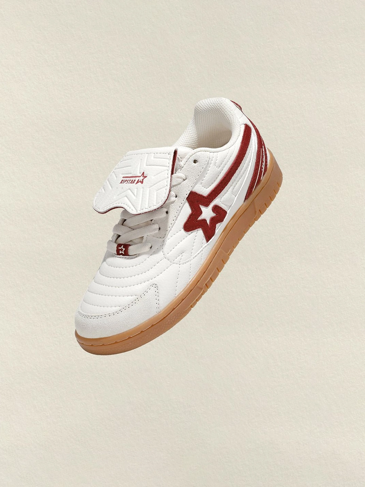 Single rice red star panel retro court sneaker angled overhead showing fold-over layered tongue, suede star panel and gum sole