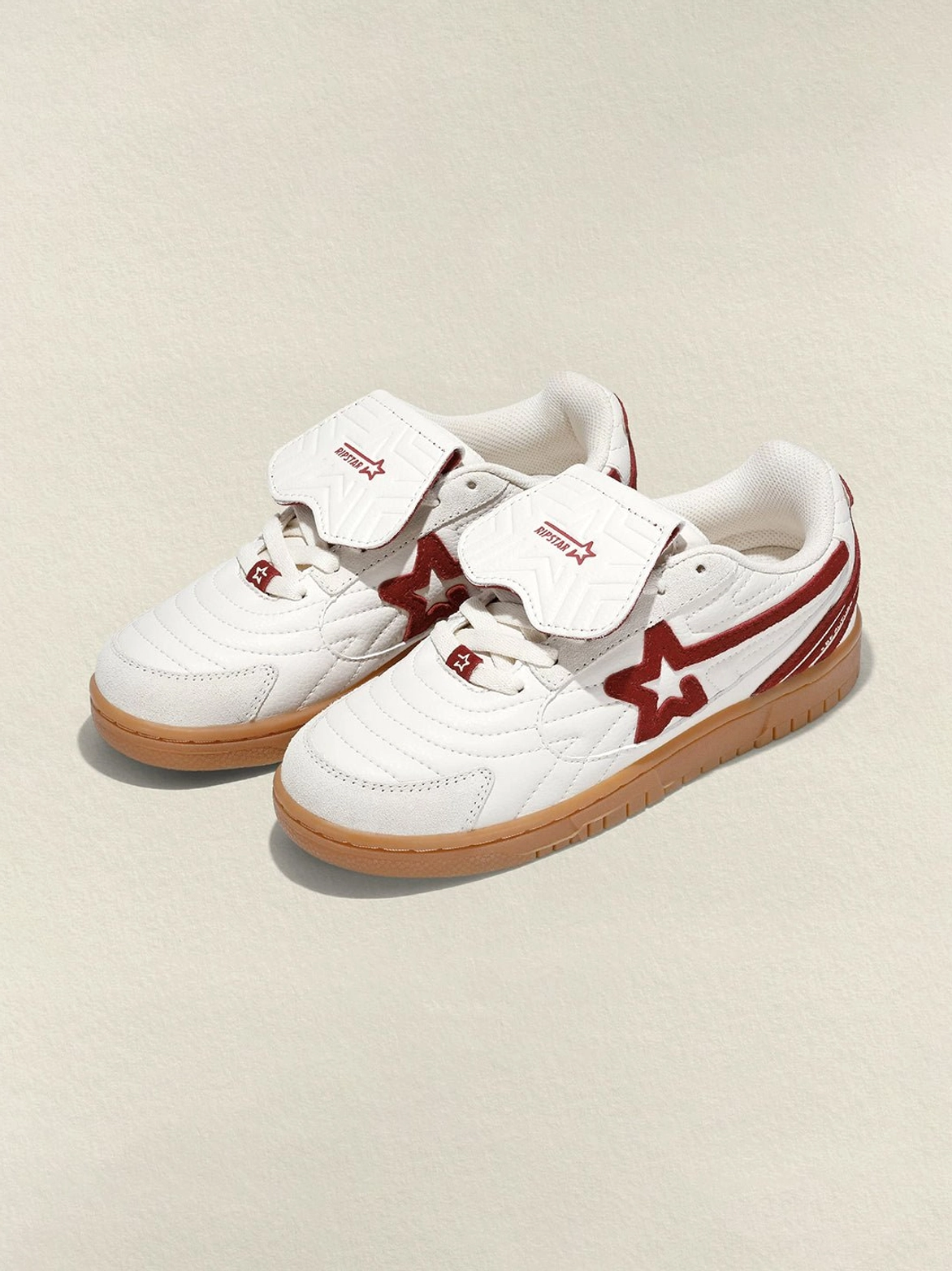 Overhead view of matching rice-white wine-red star panel retro court sneakers with layered tongues and gum rubber soles