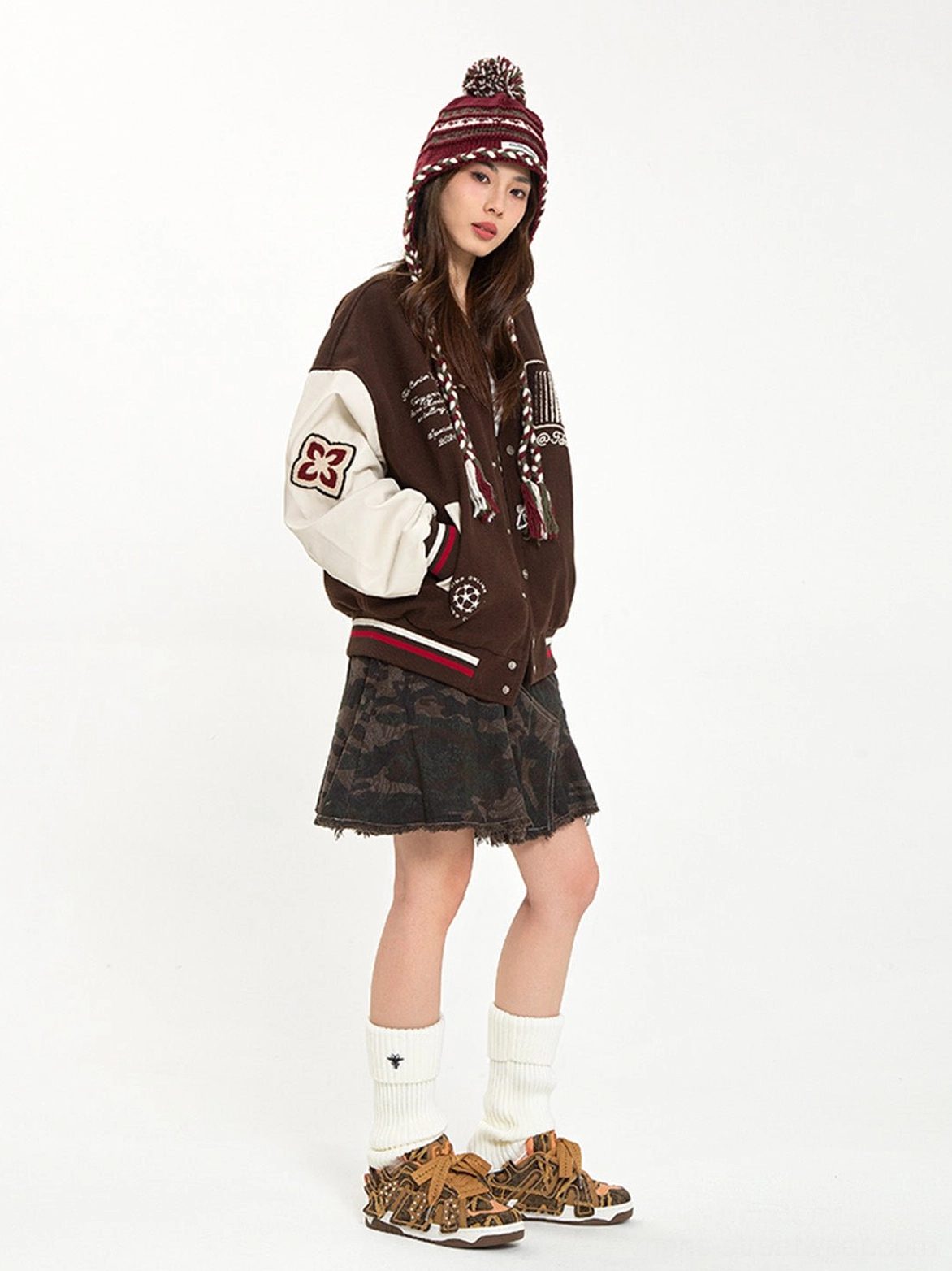 Female model in vintage varsity streetwear showing brown camouflage rivet platform skate sneakers from a front three-quarter view