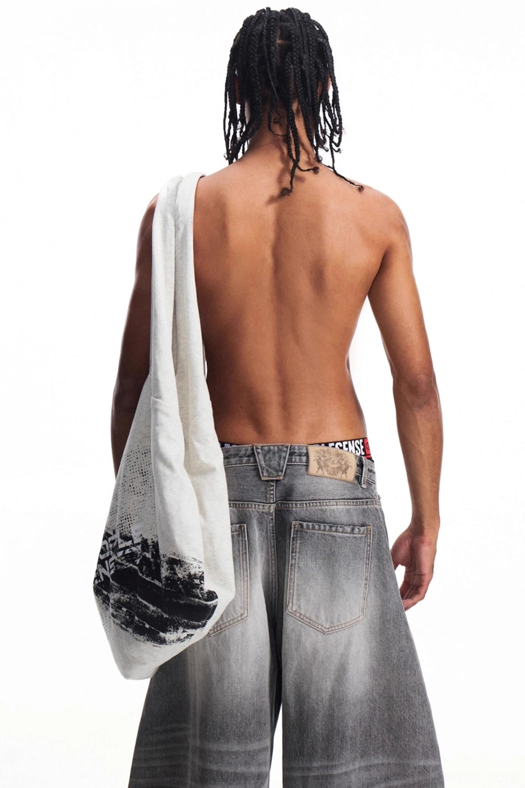 Rear view of a roomy distressed canvas tote bag showing the side graphic print with loose gray denim streetwear