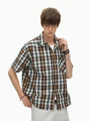 Male model wearing a rust coffee plaid boxy short-sleeve shirt with light gray trousers in a three-quarter studio view