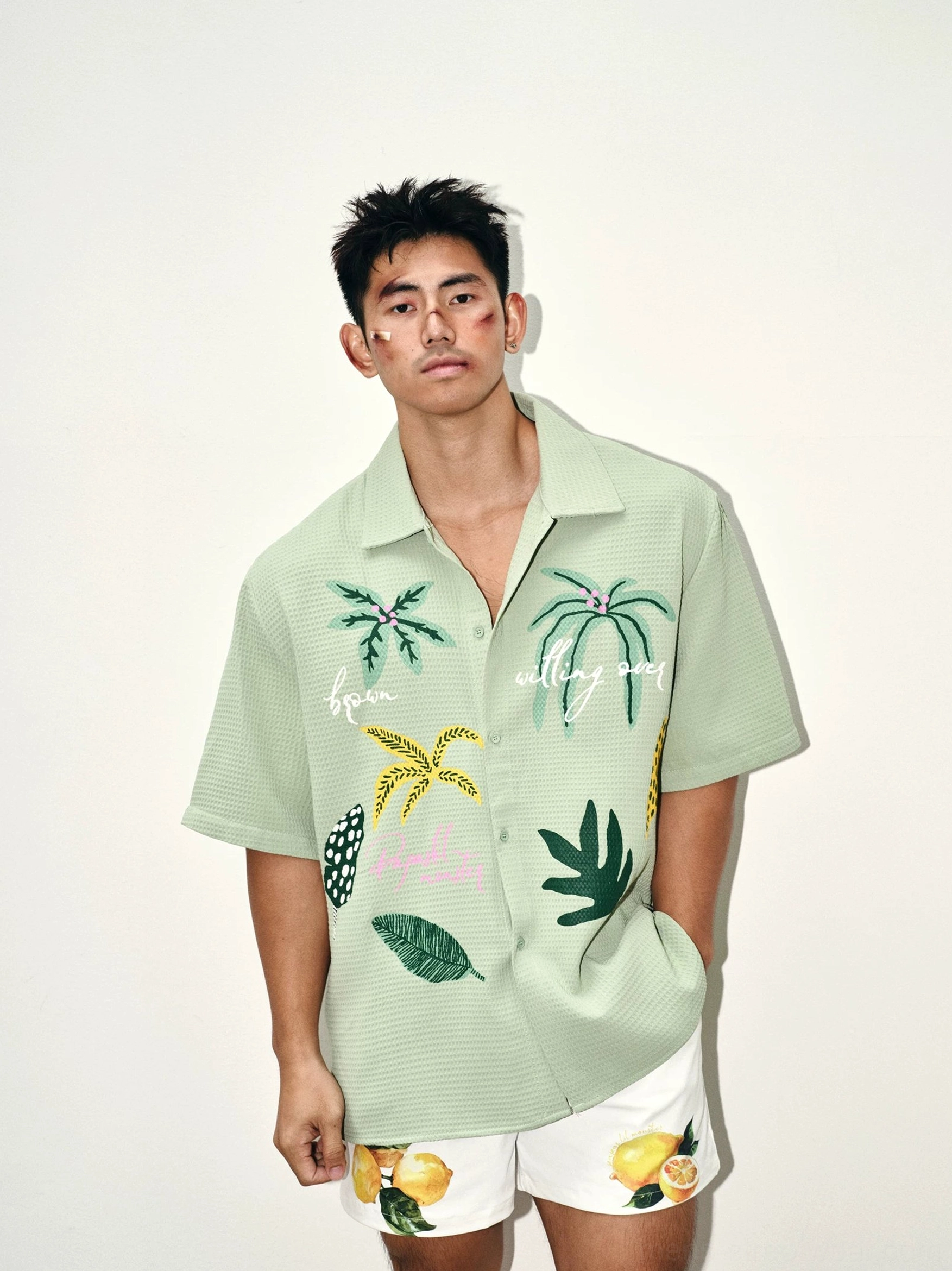Front waist-up view of sage green tropical embroidered waffle camp shirt with palm graphics and relaxed summer streetwear styling