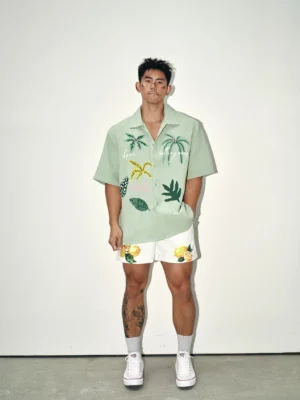 Male model wearing sage green tropical waffle embroidered camp collar shirt with palm graphics and patterned summer shorts front view