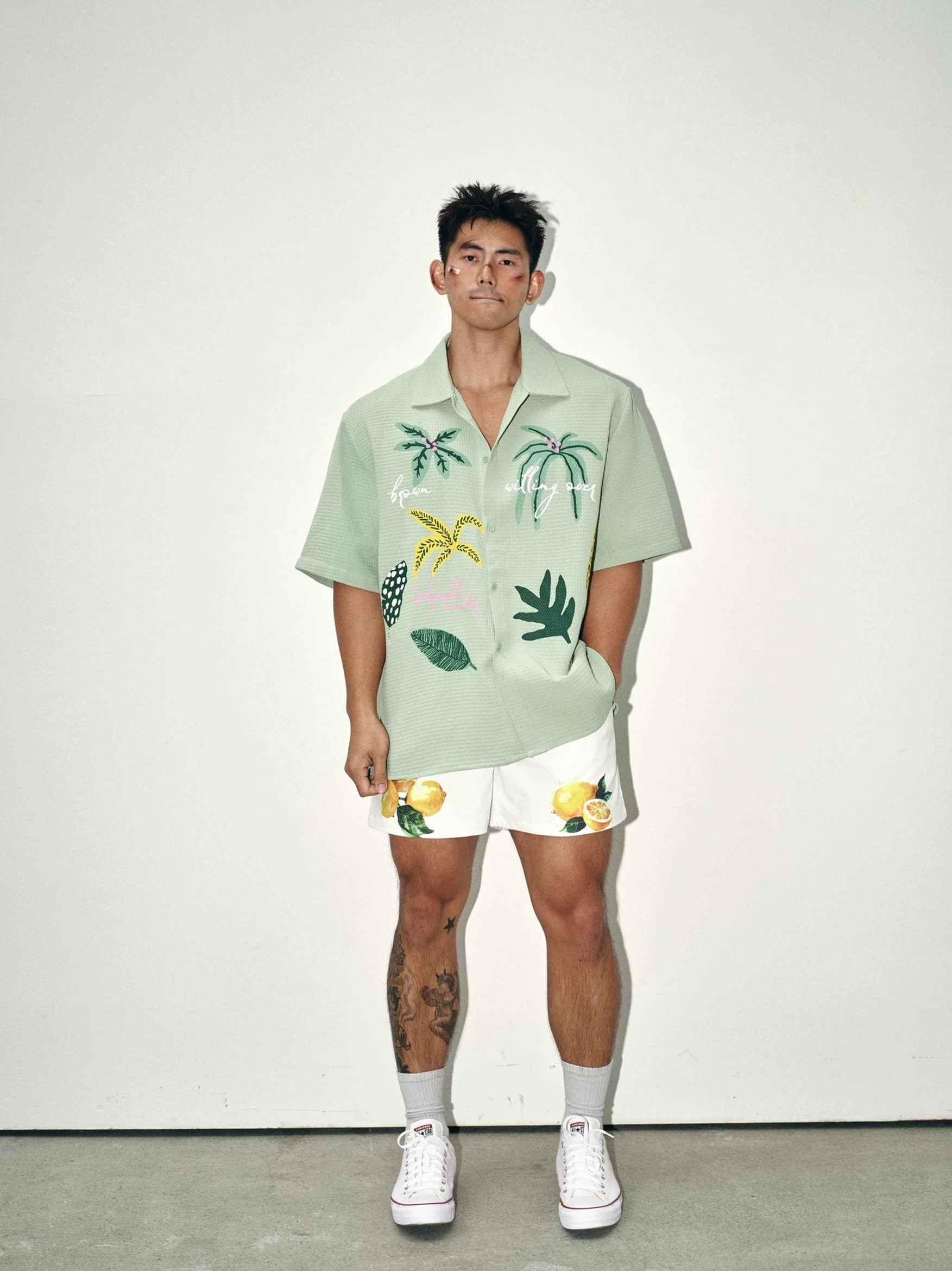Male model wearing sage green tropical waffle embroidered camp collar shirt with palm graphics and patterned summer shorts front view