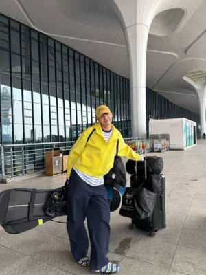 Yellow sculpted boxy full-zip hoodie worn in a side view with dark wide-leg pants in an airport terminal