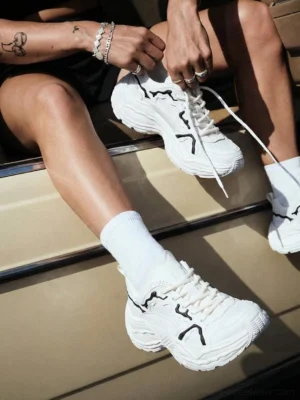 White sculpted leather chunky streetwear sneakers worn with white socks in a casual urban lifestyle setting
