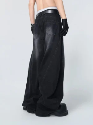 Rear oblique view of wide-leg black streetwear jeans showing double back pockets, curved oversized legs, and faded charcoal denim wash