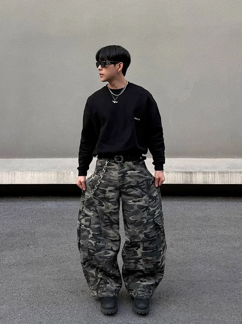 Left front view of grey camouflage balloon cargo pants styled with black sweatshirt, sunglasses, layered necklaces, and urban streetwear accessories