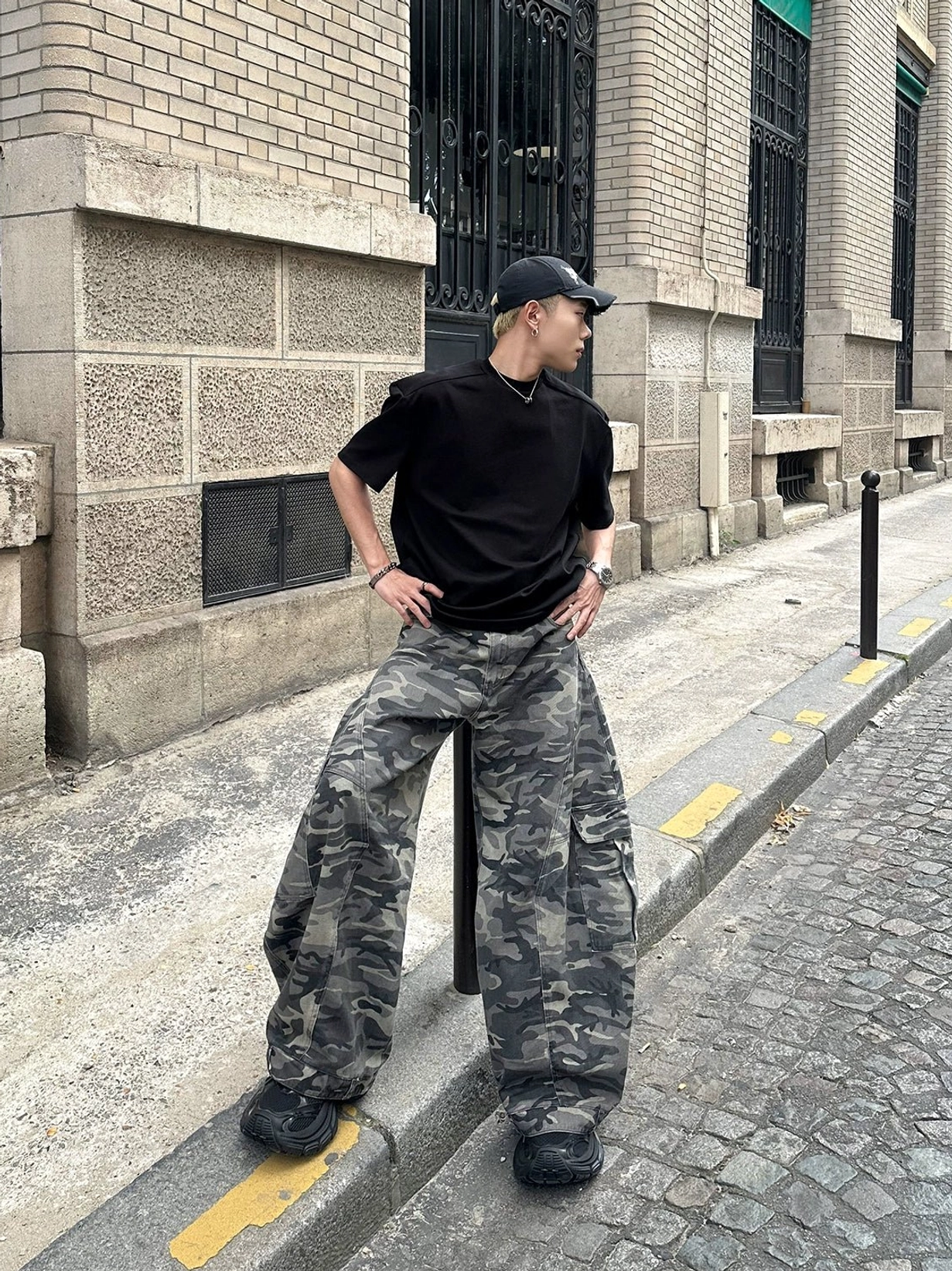 Outdoor side full-body view of grey camo wide-leg cargo pants featuring oversized silhouette and utility pocket detailing