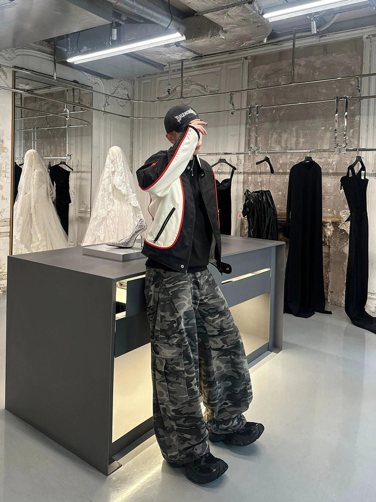 Back three-quarter view of grey camouflage loose-fit cargo pants with wide legs and dimensional side utility pockets in a boutique setting