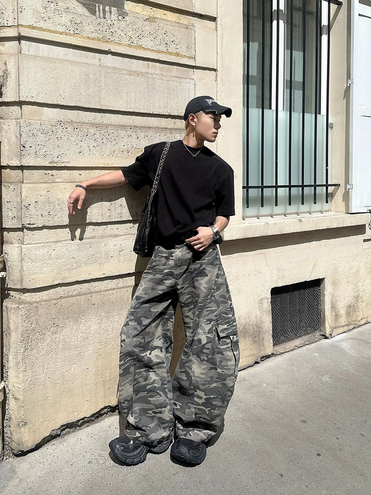 Side outdoor view of washed grey camouflage wide-leg cargo pants with oversized utility pockets styled with a black t-shirt and sneakers