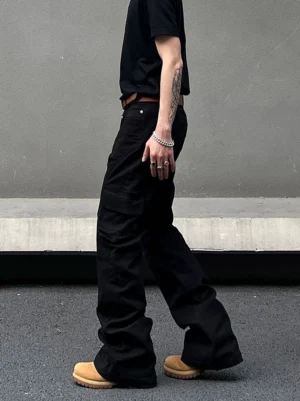 Side walking view of black cargo flared pants showing stacked hems, utility pockets, brown leather belt, and tan work boots