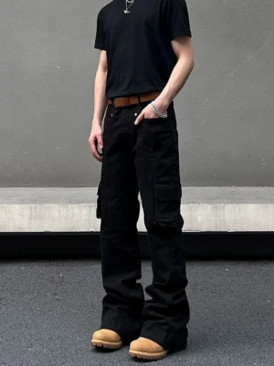 Front view of black flared cargo pants with multiple side pockets styled with a black T-shirt and silver jewelry in an industrial streetwear setting