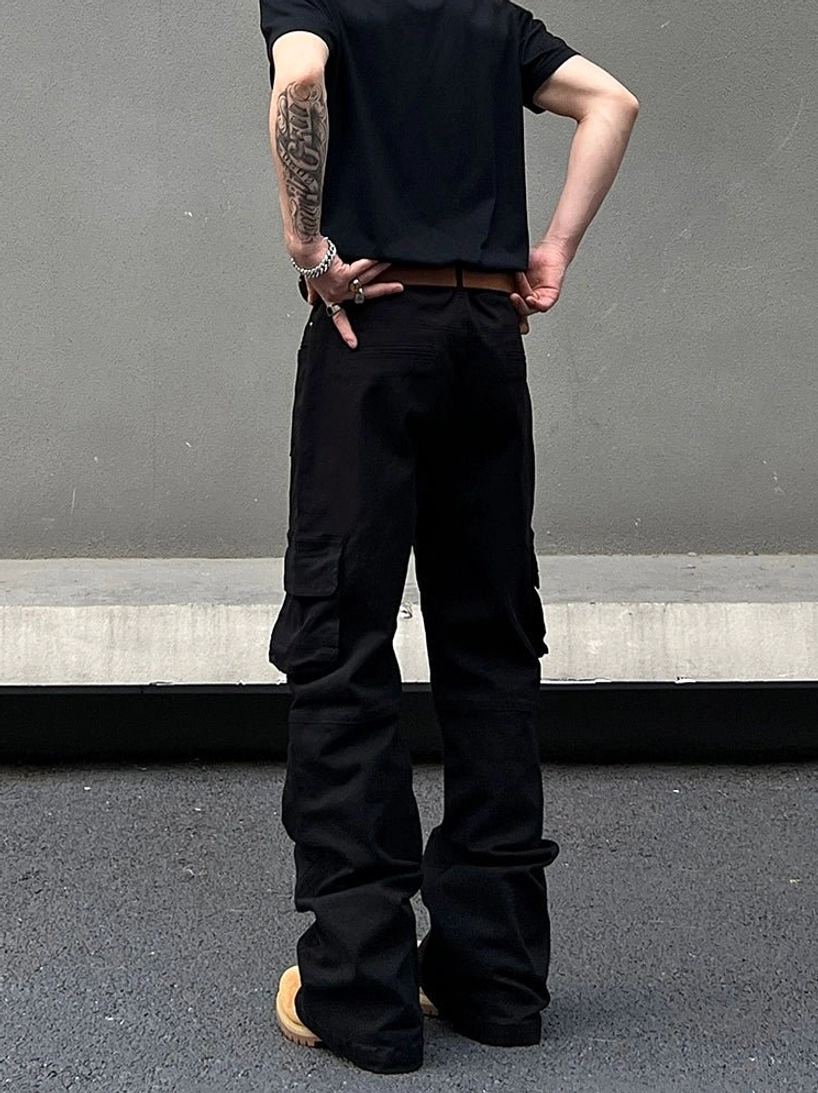 Rear view of black flared cargo pants showing back pockets, wide leg shape, stacked hem, and industrial streetwear styling