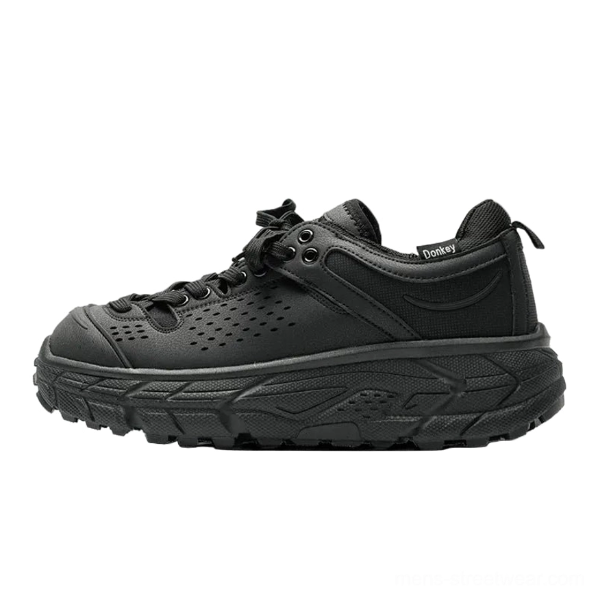 Side profile of a single charcoal black utility trainer with perforated toe box, padded heel tab, chunky midsole, and adjustable laces