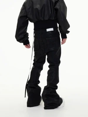 Back view of men's black stacked flare jeans showing dual rear patch pockets, waistband detail, hanging side strap, and dramatic ankle stacking