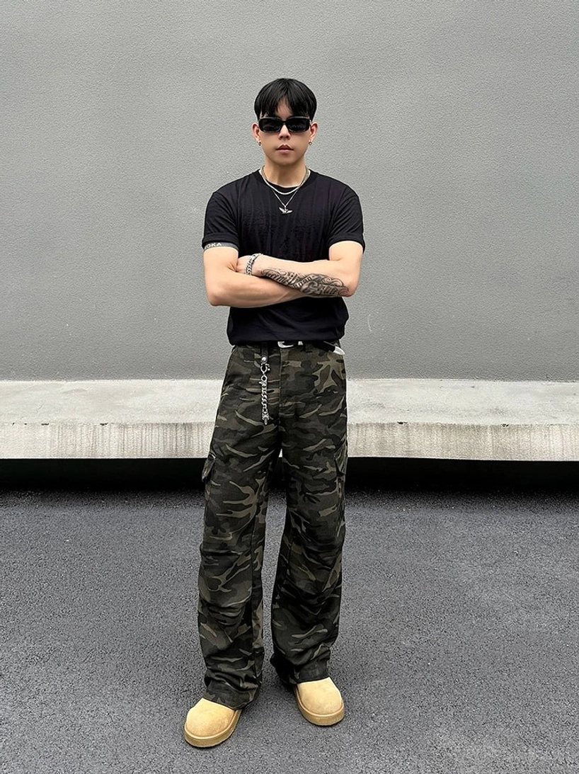 Front view of dark woodland camouflage streetwear cargo pants with loose wide-leg silhouette in industrial outdoor setting
