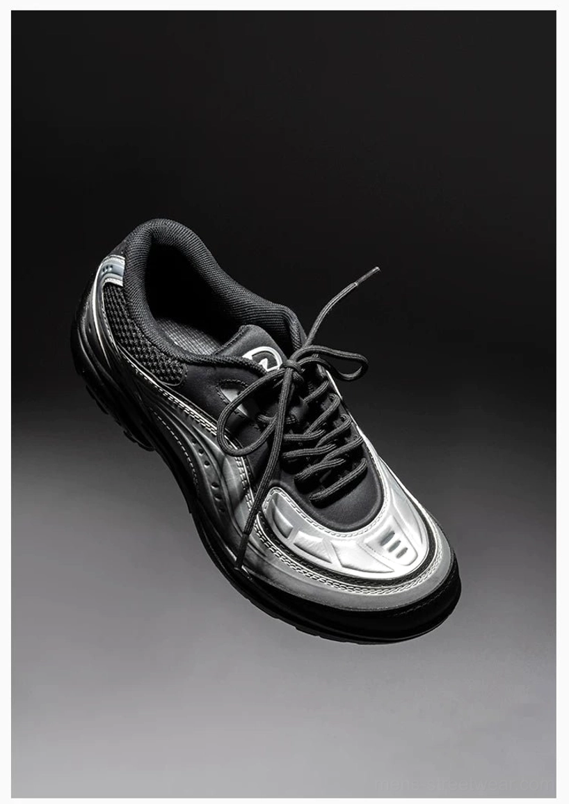 Close-up front three-quarter view of a silver black streetwear sneaker with glossy metallic panels, black laces, mesh details, and padded tongue