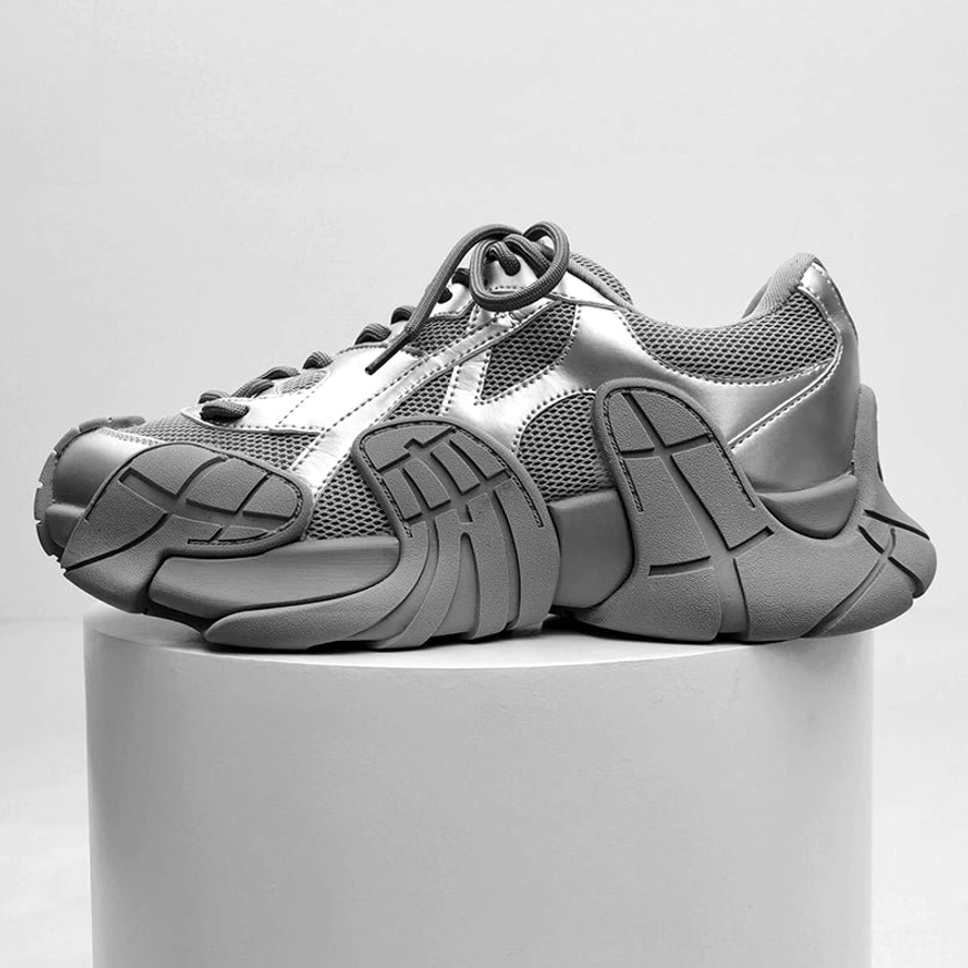 Silver and dark grey futuristic chunky platform sneaker displayed on a pedestal, mesh fabric panels and textured thick outsole