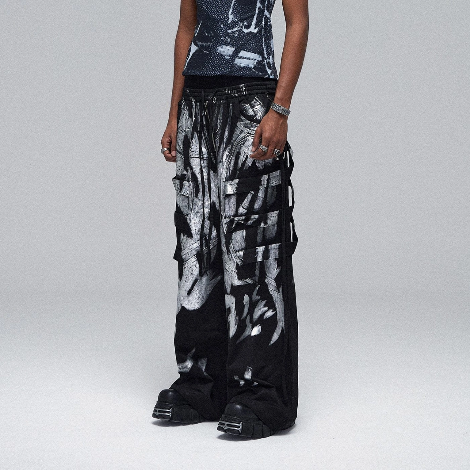 Side view of silver graffiti print cargo pants with multiple utility pockets, adjustable side drawstrings, and chunky boot styling
