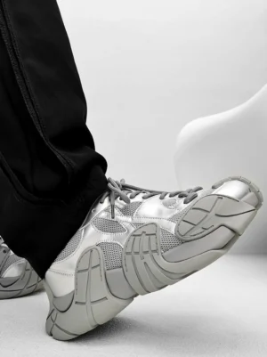 Silver and light grey futuristic chunky platform sneakers worn with loose black street trousers, layered mesh panels, and segmented textured sole