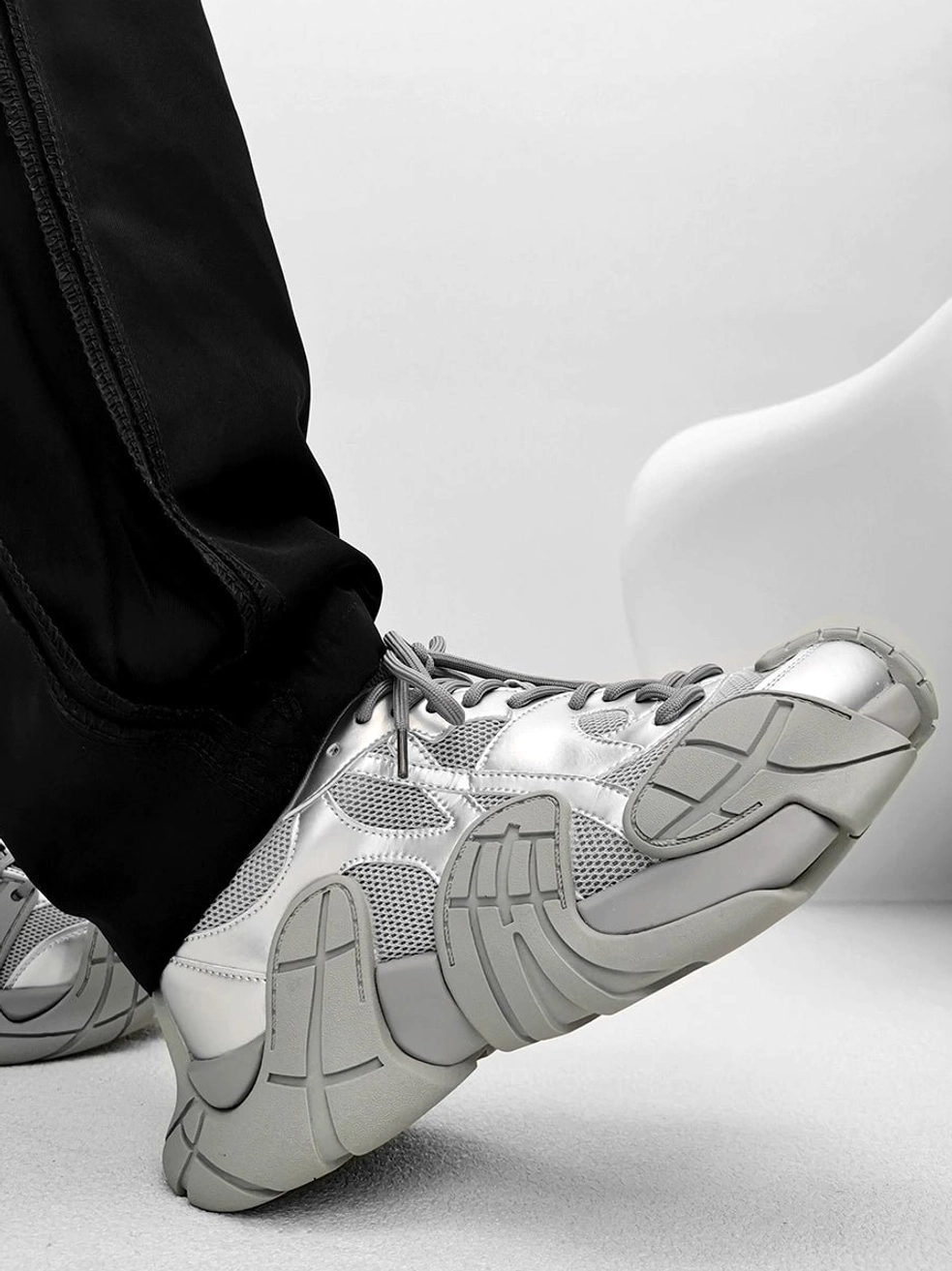 Silver and light grey futuristic chunky platform sneakers worn with loose black street trousers, layered mesh panels, and segmented textured sole