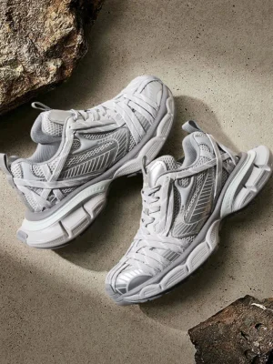 Pair of silver grey layered mesh chunky runner sneakers shown from above on a textured concrete surface