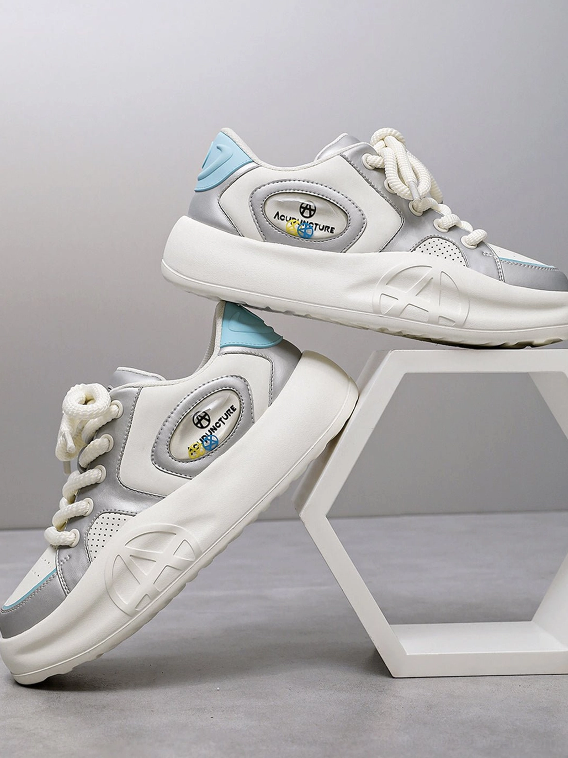 Silver metallic chunky platform sneakers displayed on a geometric stand, highlighting the side detail and layered white outsole