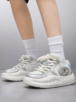 Model wearing silver metallic platform sneakers with white crew socks in a low angle front view, showing lace-up design and chunky streetwear silhouette