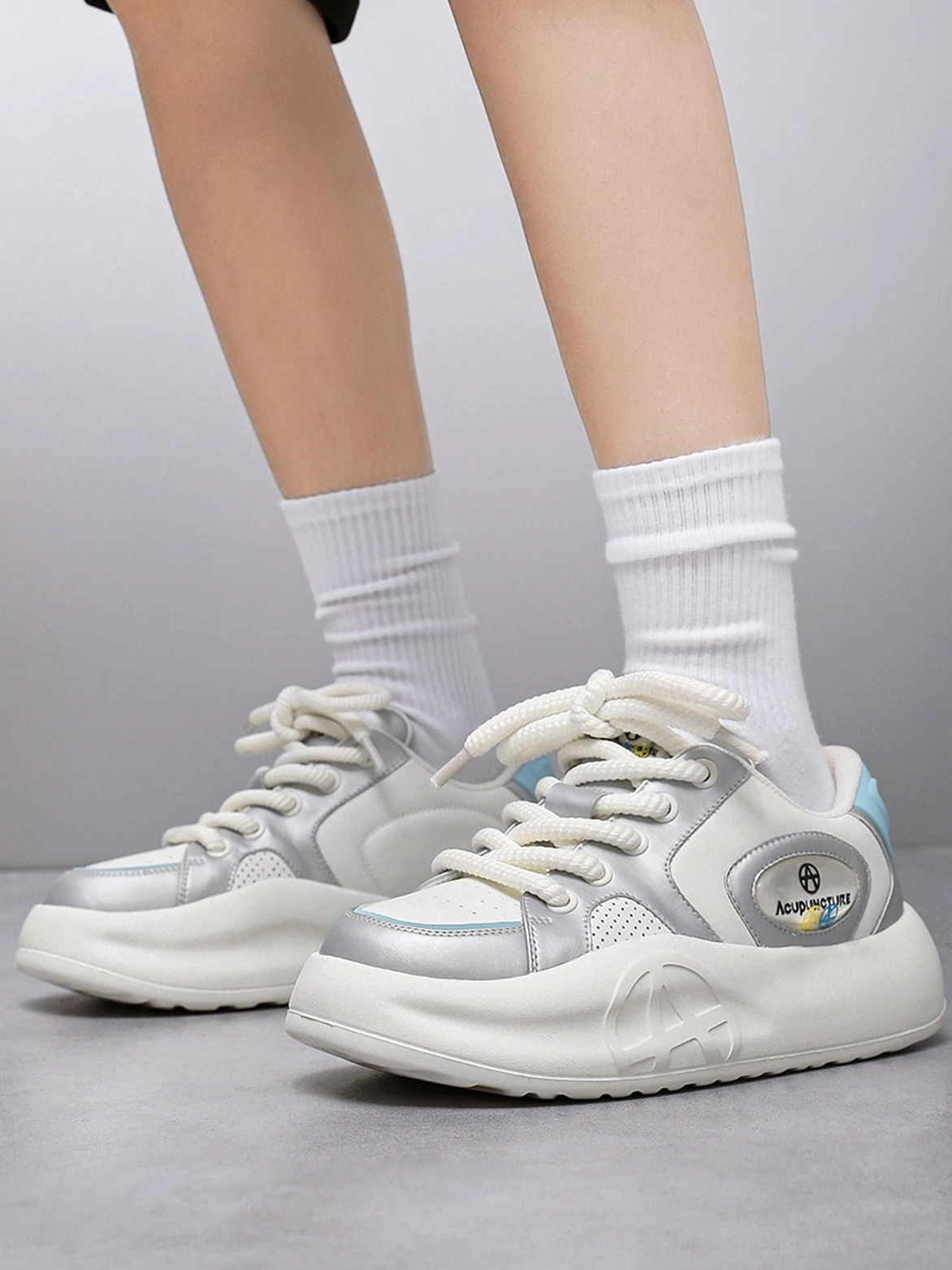 Model wearing silver metallic platform sneakers with white crew socks in a low angle front view, showing lace-up design and chunky streetwear silhouette