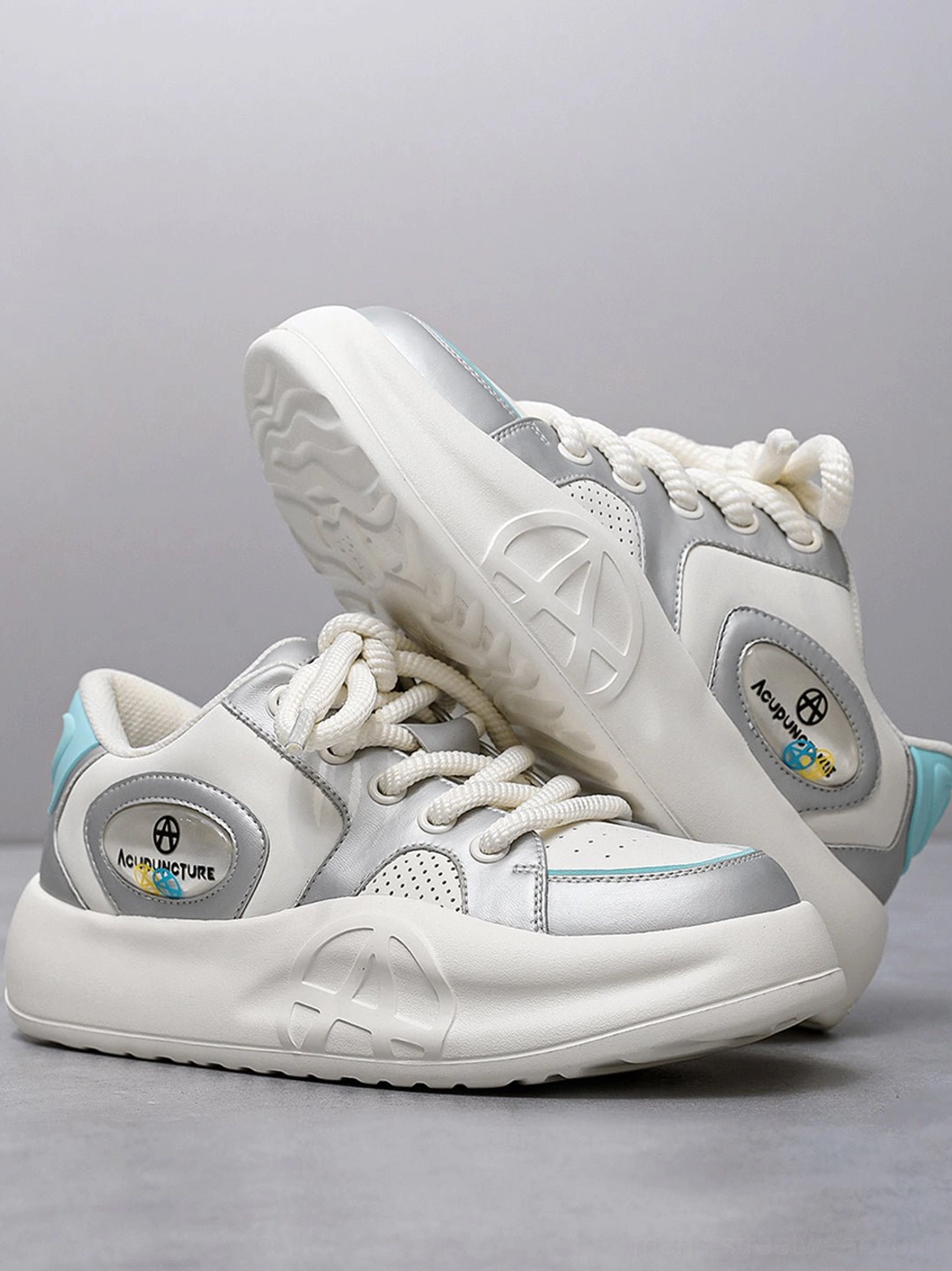 Overhead view of silver metallic platform sneakers with thick round laces and one shoe flipped to reveal the embossed outsole