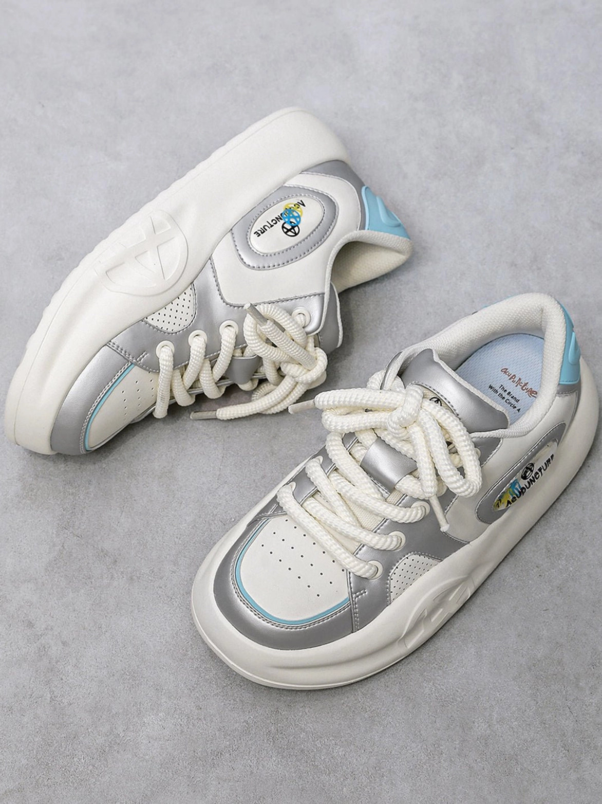 Side and sole view of silver metallic platform sneakers showing inner shoe details, light blue heel accent, side patch, and chunky outsole