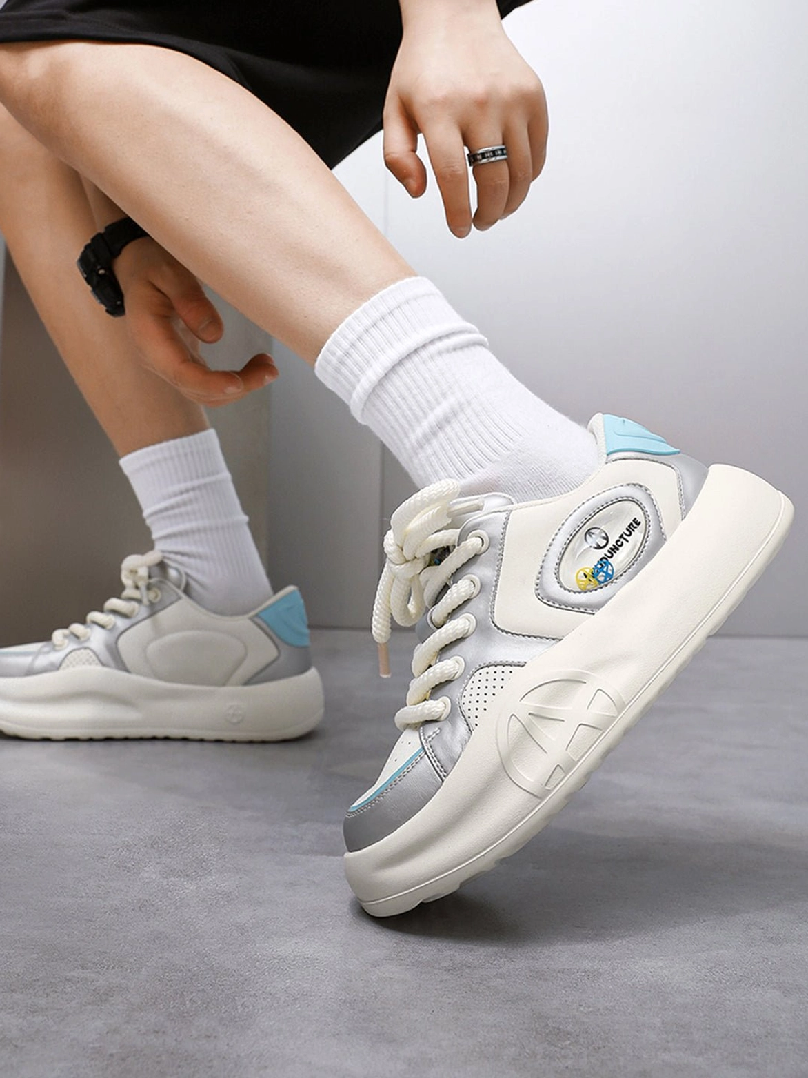 Three-quarter view of silver metallic platform sneakers worn with black shorts and white socks, showing side patch and raised outsole