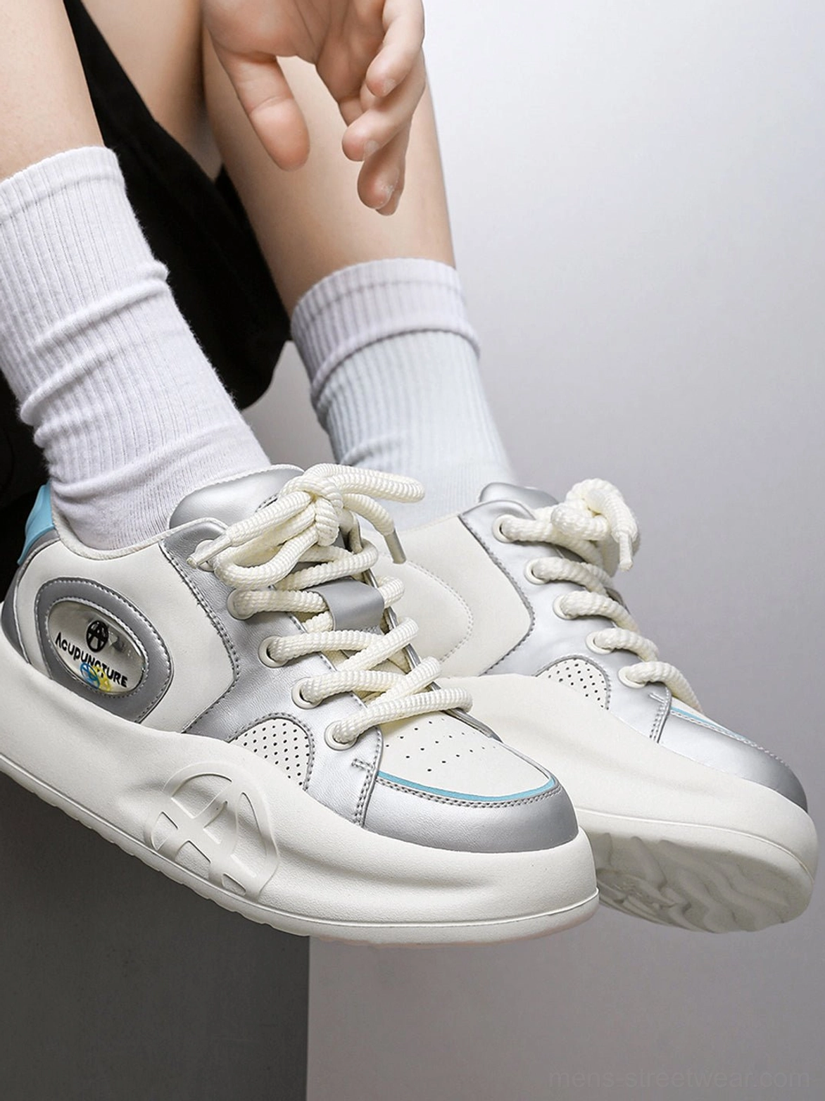 Close-up of silver metallic streetwear sneakers with light blue heel accent, decorative side patch, and thick white platform outsole