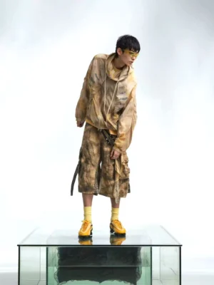 Three-quarter view of a relaxed skeleton print tie dye windbreaker jacket with earthy brown tones, cargo shorts, utility styling, and yellow sneakers