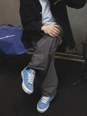 Male streetwear outfit wearing sky blue embroidered skate sneakers with black coat, white tee, and relaxed gray pants