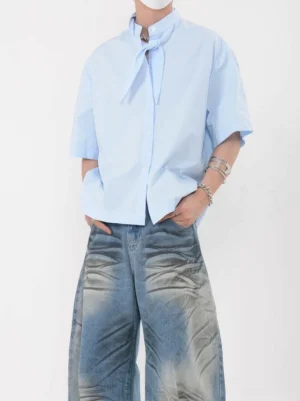 Full-body view of a sky blue short sleeve knot collar shirt with boxy oversized silhouette, front button closure, and wide-leg denim styling