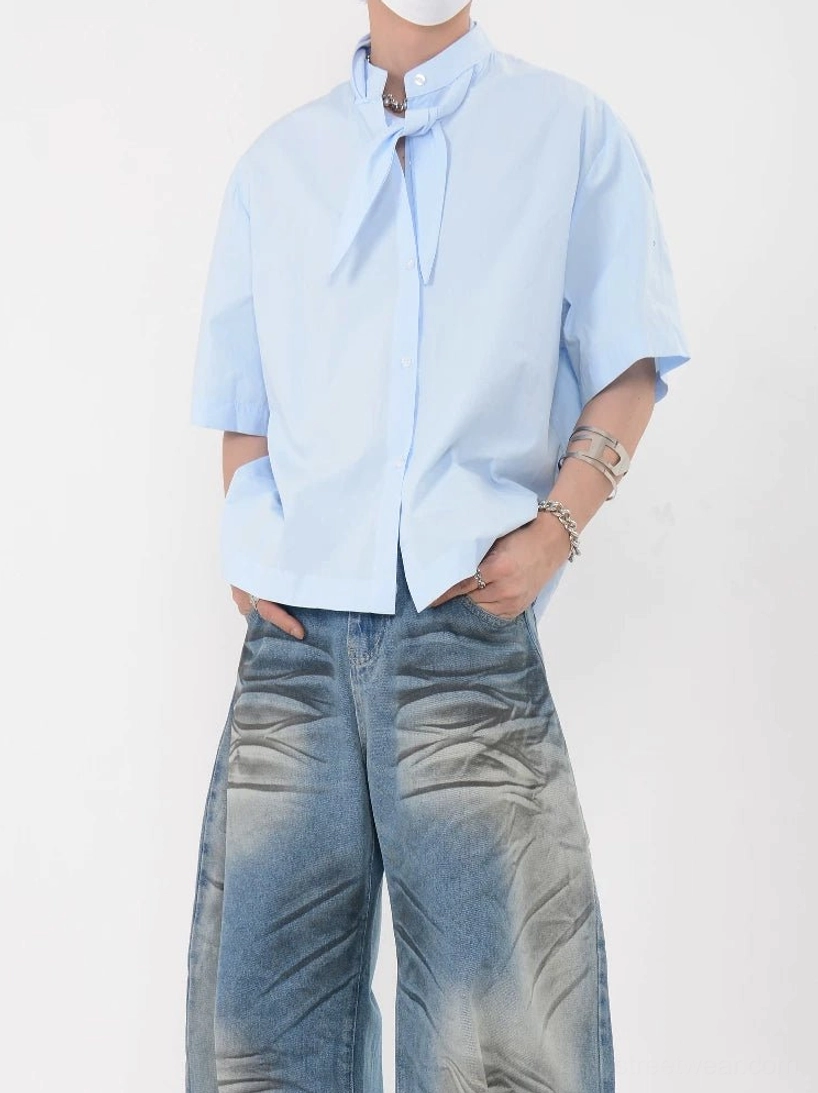 Full-body view of a sky blue short sleeve knot collar shirt with boxy oversized silhouette, front button closure, and wide-leg denim styling