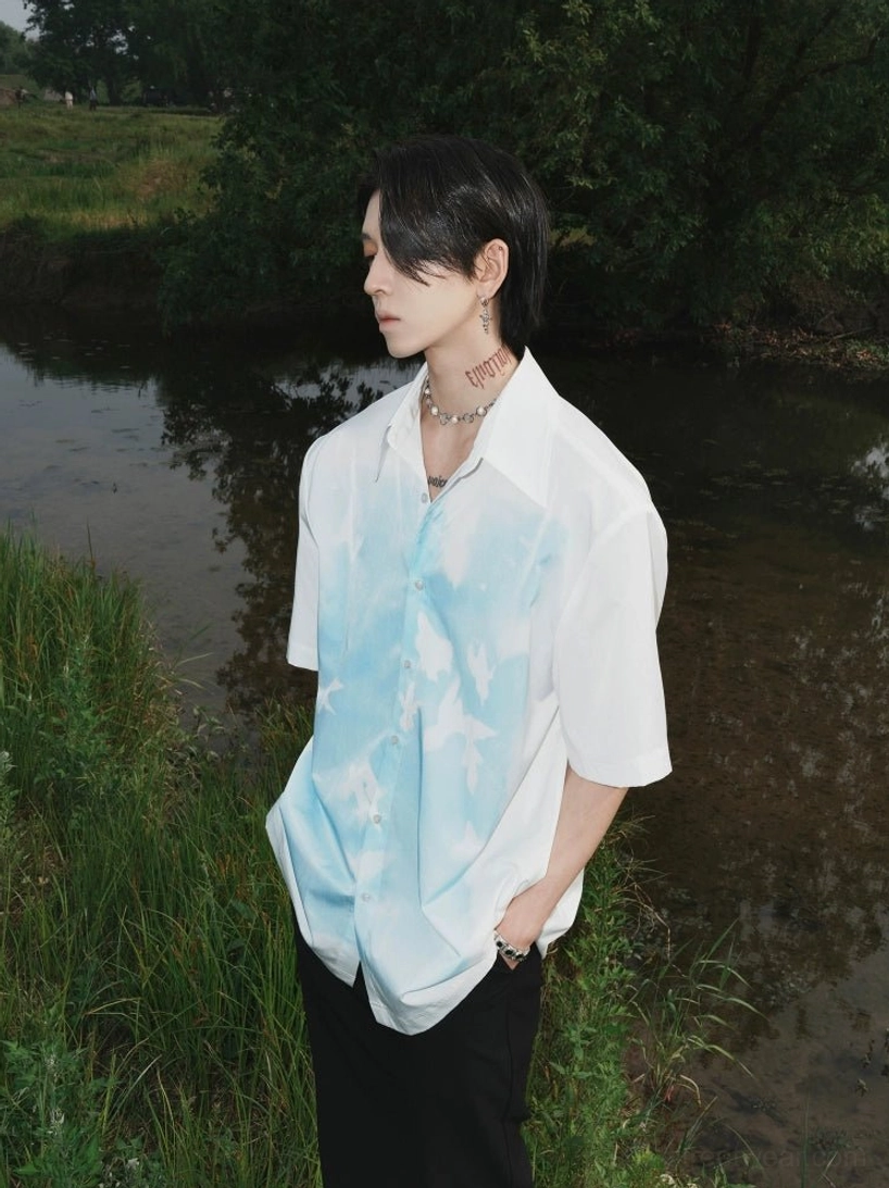 Skybound Doves Dream relaxed sky print button shirt on male model in waterside grassland left side view