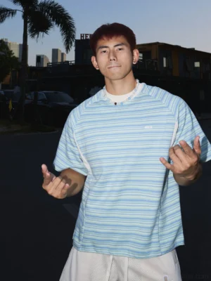 Light blue skyline ripple striped raglan streetwear tee front view worn outdoors on a palm-lined urban street