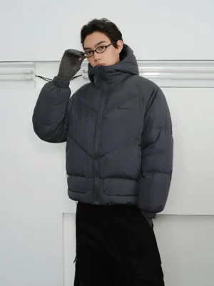 Men's slate grey hooded puffer jacket three-quarter front view showing relaxed cropped fit ribbed cuffs and chevron quilting