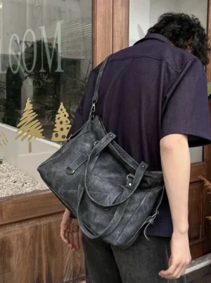 Slate vintage panel tote bag worn over the shoulder by a male model in a dark purple shirt outside a retro storefront