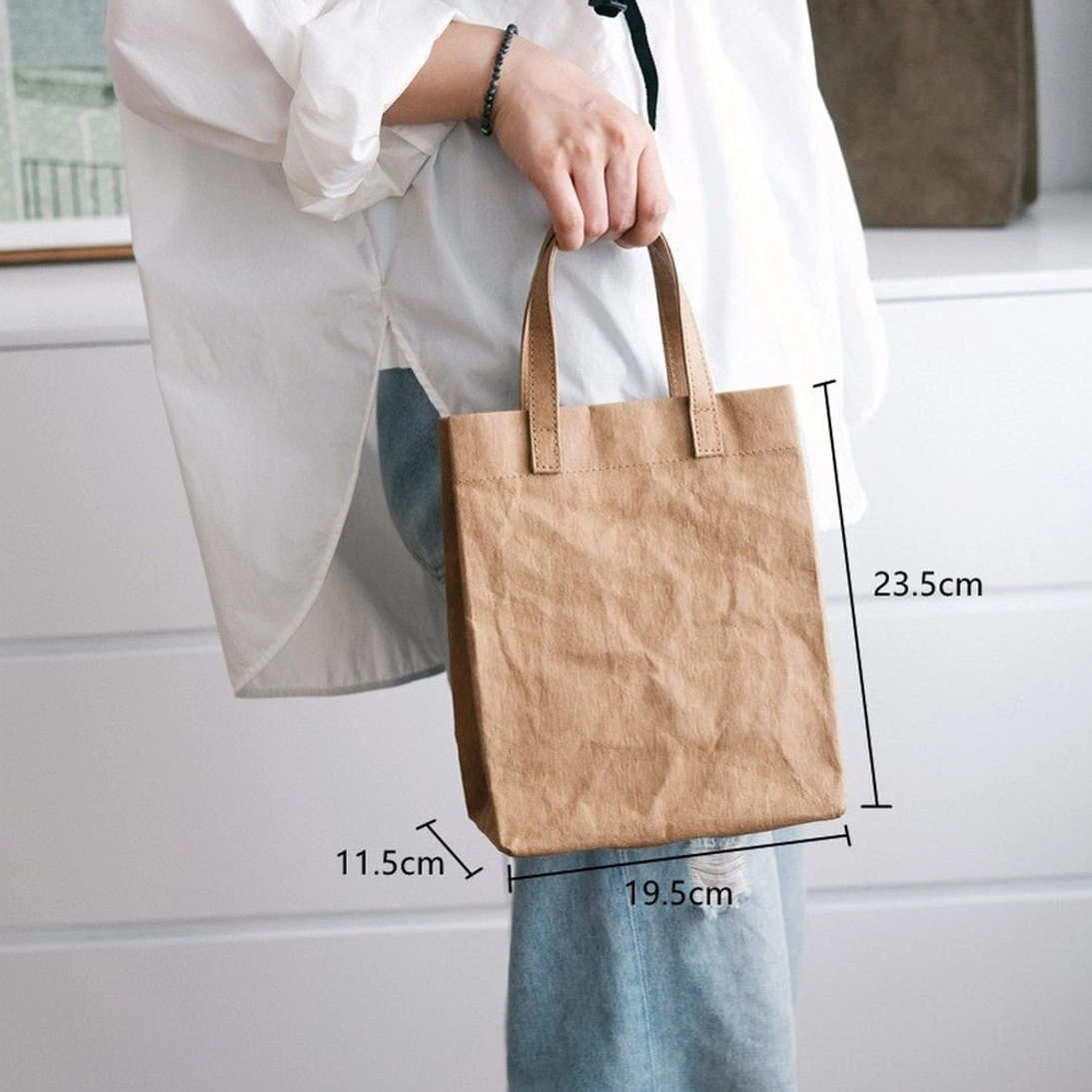 Small khaki faux kraft paper cotton tote bag worn at waist level showing compact rectangular shape and dimensions