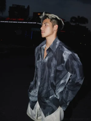 Side profile of a male model wearing a smoky monochrome abstract satin oversized shirt with relaxed long sleeves and open neckline