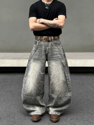 Model wearing vintage smoky gray baggy jeans with white paint splatters, relaxed oversized balloon fit, faded denim texture, black tee, and streetwear accessories