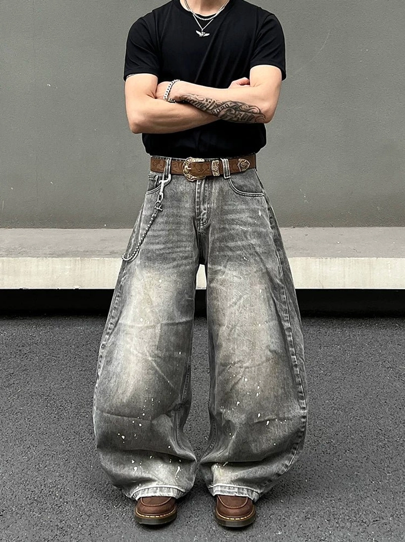 Model wearing vintage smoky gray baggy jeans with white paint splatters, relaxed oversized balloon fit, faded denim texture, black tee, and streetwear accessories