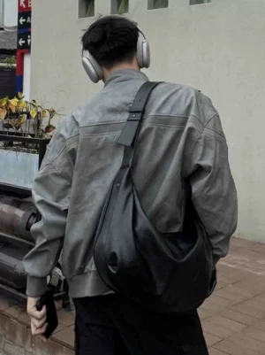 Back three-quarter view of a male model wearing the black Soft Drape Luna Hobo shoulder bag with a gray jacket and headphones in an urban street setting