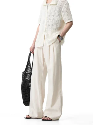 Side view of cream relaxed wide-leg trousers with a hollow knit shirt, mesh tote bag and slide sandals